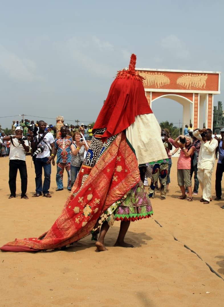 An Egungun in an embroidered red costume before the Door of No Return in Ouidah