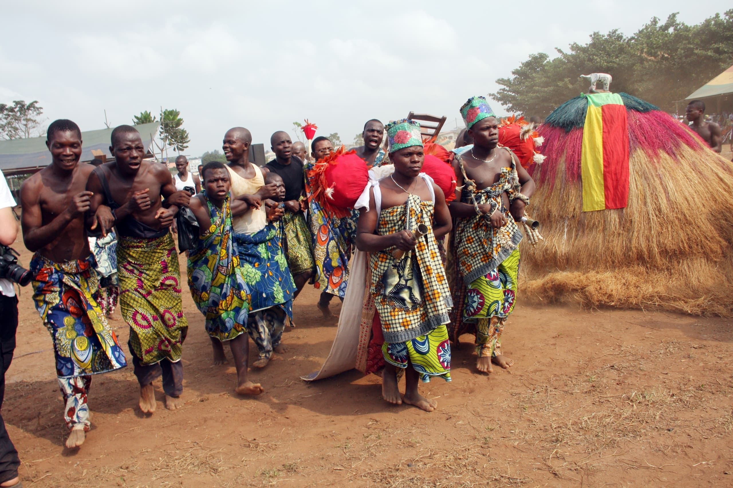 Danseurs en pagnes colorés devant un Zangbeto